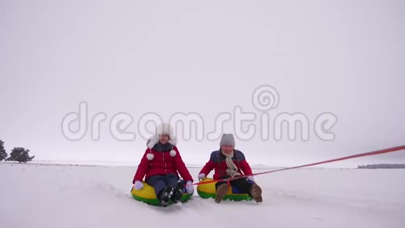 快乐的女孩在冬天的雪地里雪橇挥舞着双手孩子们在充气的雪管上滑动大笑和视频的预览图