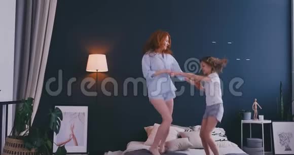 漂亮的妈妈和女儿在家里跳床时玩得很开心视频的预览图