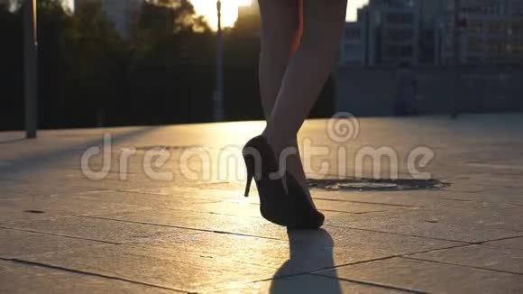 在日落时分穿着高跟鞋沿着城市街道行走的女性腿穿高跟鞋的年轻女商人视频的预览图