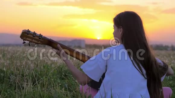 小女孩弹吉他日落时美丽的夏季景观艺术音乐概念镇附近的蒲公英田视频的预览图