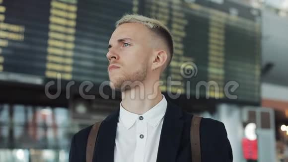 迷人的年轻商人在机场的时刻表屏幕附近等朋友他挥手开会视频的预览图