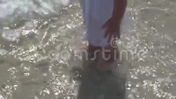 一个孩子赤脚在水中行走婴儿在海水中的海滩上台阶视频的预览图