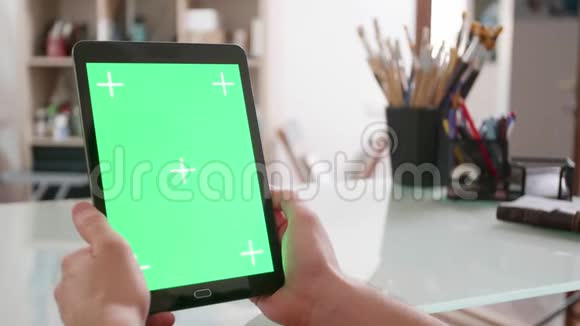 年轻的艺术家在他的工作室里看平板电脑的绿色屏幕视频的预览图