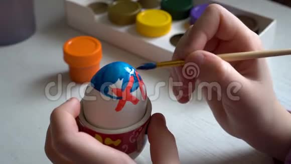 孩子坐在桌子旁画一个刷复活节彩蛋的蓝色和红色颜料快关门4K25fps视频的预览图