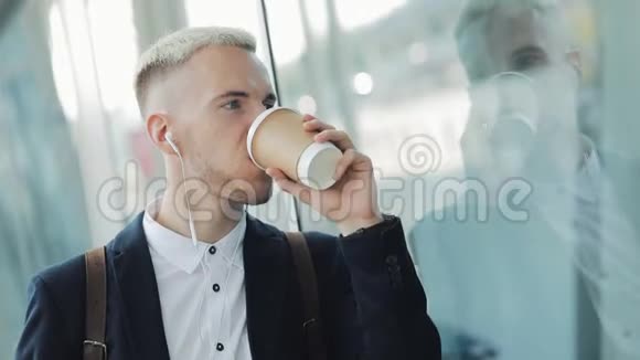 年轻商人拿着咖啡对着镜头喝着热饮的画像他听音乐笑视频的预览图