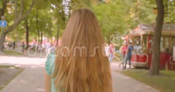 特写后景照片年轻的长发美丽的女性走着在户外公园里看着相机视频的预览图