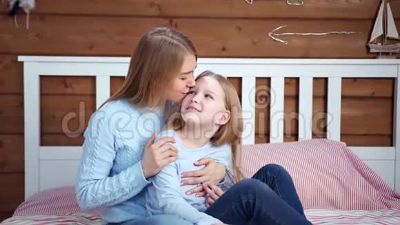 幸福的家庭年轻的母亲和可爱的小女儿微笑着拥抱坐在床上视频的预览图