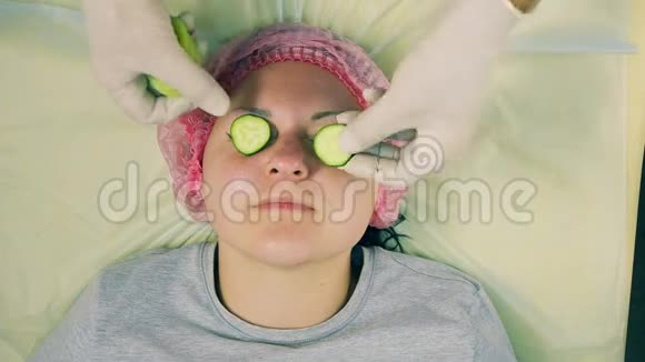 戴手套的男性美容师的双手将猕猴桃和黄瓜的面具戴在女人脸上视频的预览图