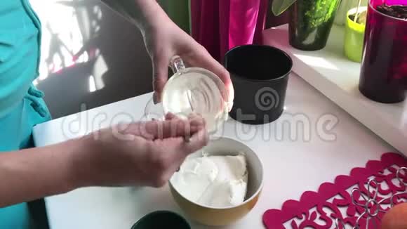 女人在奶酪里加入酸奶油蓝莓芝士蛋糕烹饪材料位于桌子表面视频的预览图