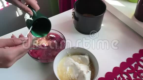 女人在干酪中加入溶解的明胶蓝莓芝士蛋糕烹饪原料位于ta表面视频的预览图