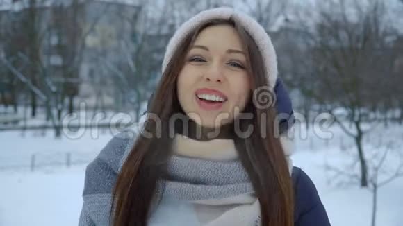 冬天在公园里穿着温暖的冬衣笑着的年轻女孩的肖像视频的预览图