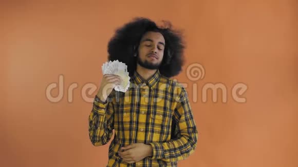 满意的非裔美国人手里拿着钞票的扇子一边孤立地站着一边看着摄像机视频的预览图
