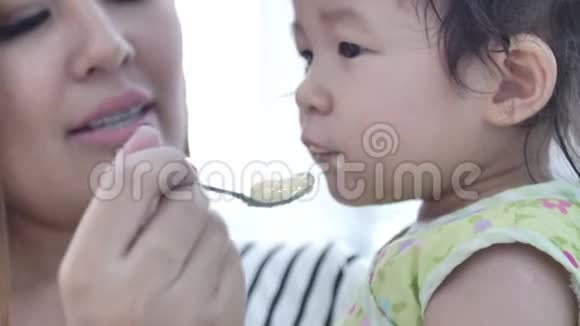 亚洲母亲在家为女儿喂饭面带微笑幸福的亚洲家庭理念视频的预览图