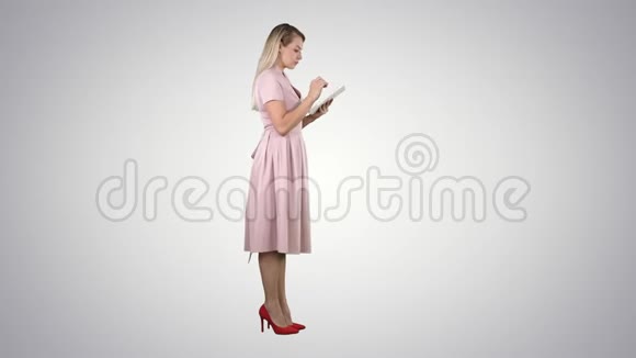 年轻女性穿着粉红色衣服的侧面视图使用平板电脑的梯度背景视频的预览图