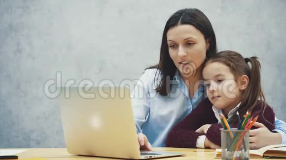 妈妈和女儿坐在桌子旁一起玩个愉快的笔记本电脑关系概念视频的预览图