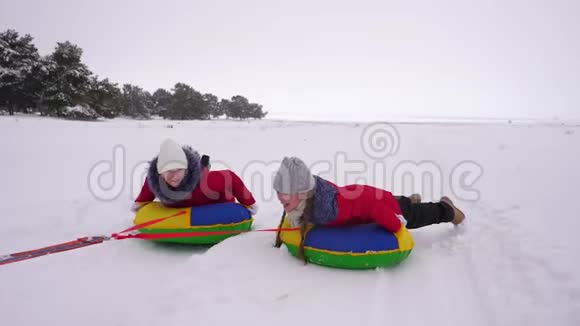 冬天穿红色夹克的孩子们骑着充气雪管和雪橇在雪中穿行运动女孩放松视频的预览图