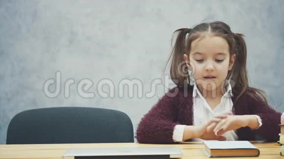 一个女学生坐在桌子旁在此期间选择一本书或笔记本电脑在灰色背景下快乐开启视频的预览图