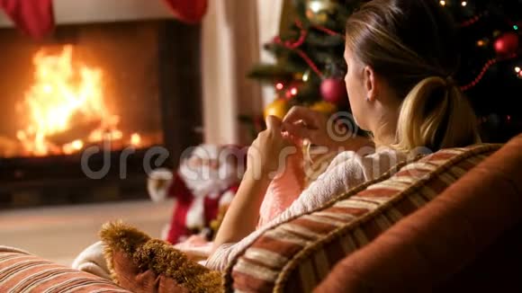 在燃烧的壁炉和圣诞树上编织羊毛围巾的年轻女子4k镜头视频的预览图