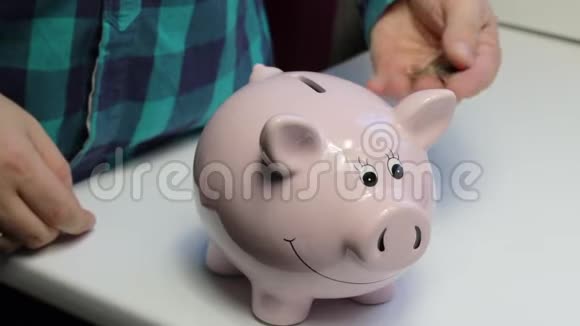 桌子上有一只粉红色的猪形的储蓄罐那个人手里拿着一枚硬币他把它依次放进一只小猪b里视频的预览图