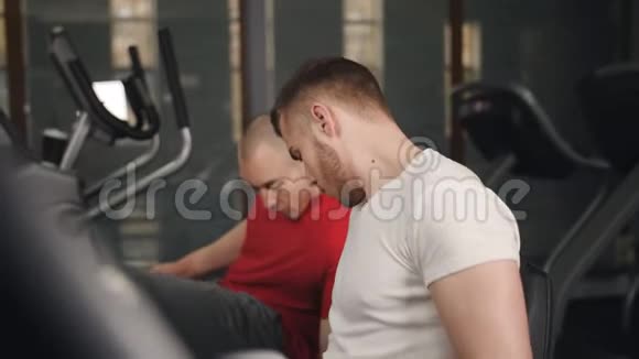 两个人在健身房骑自行车锻炼他的腿做有氧训练骑自行车视频的预览图