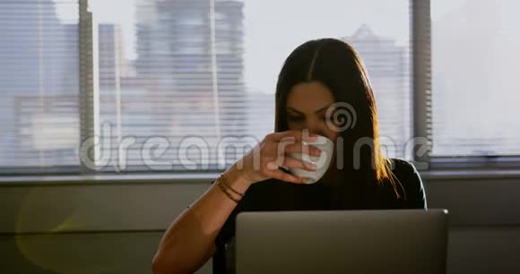 年轻的高加索女商人在办公室工作时喝咖啡的正面景色视频的预览图