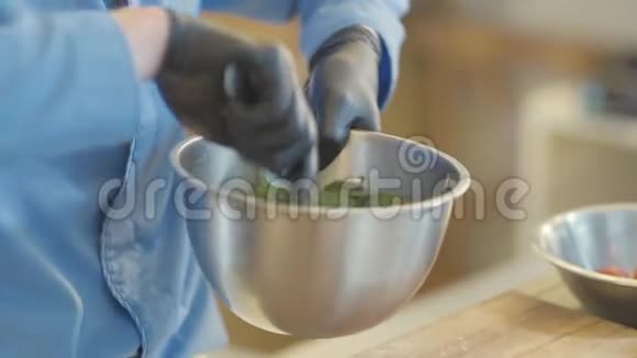 专业厨师手戴黑色橡胶手套用勺子把沙拉和调味料混合在铝碗里视频的预览图