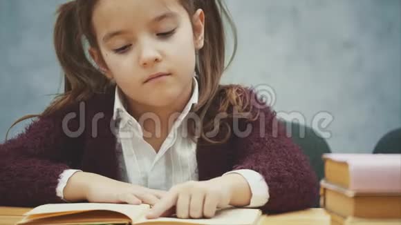 灰色背景上可爱的小女孩坐在桌子上读一本书视频的预览图
