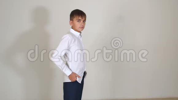 一个穿着白色衬衫的小男孩站在白色的背景上双手插在口袋里视频的预览图