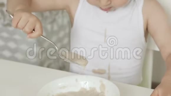 一个小女孩坐在孩子们桌子旁用勺子吃粥视频的预览图