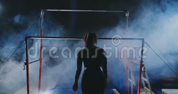 体操比赛一个女人走到横杆前在黑暗中缓慢地做着蘸水的动作视频的预览图