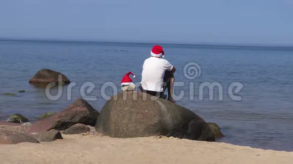 人类坐在海边的岩石上戴着圣诞老人的帽子视频的预览图