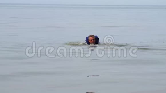 穿着蓝色救生衣的人漂浮在岸边视频的预览图