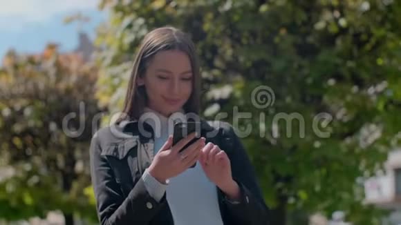 迷人的年轻女子在阳光明媚的城市街道上和朋友聊天快乐的时髦女孩在户外使用手机视频的预览图