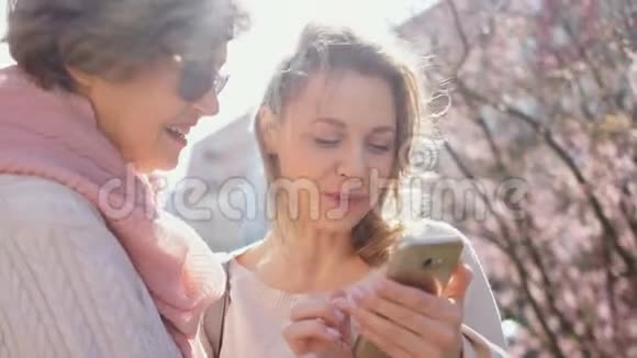 两个女人正在看一张智能手机上的照片开心地笑着妈妈和女儿站在里面说话视频的预览图