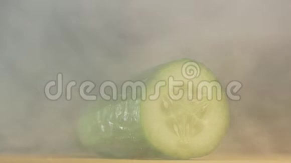 一个人用刀割着一个农夫黄瓜在雾霭和蒸发中黑色的背景特写缓慢视频的预览图