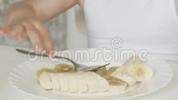 一个小女孩坐在孩子们桌子旁用叉子吃猕猴桃和香蕉视频的预览图