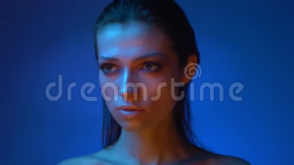 发光模型与闪光闪亮的化妆在蓝色霓虹灯观看进入相机神秘的工作室视频的预览图