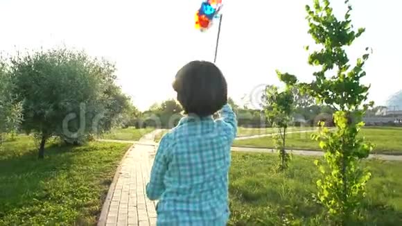 可爱的男孩手里拿着玩具风力涡轮机在夕阳下的夏季公园跑步快乐的孩子玩孩子玩得开心视频的预览图