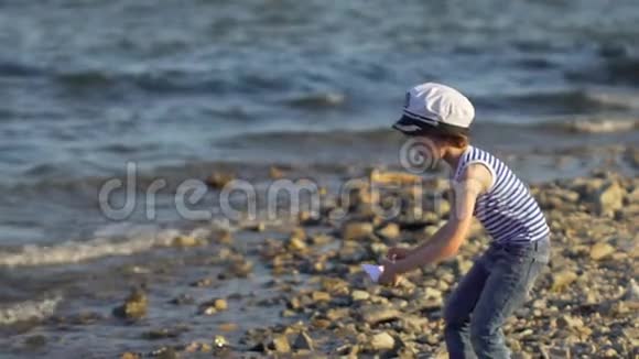 在海滩上用纸船下水的孩子小男孩把纸船放在海面上航行的船梦想未来视频的预览图