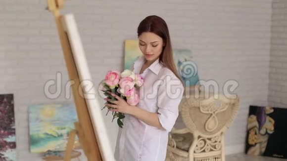 画室里有一束粉红色牡丹的美丽女孩的肖像视频的预览图