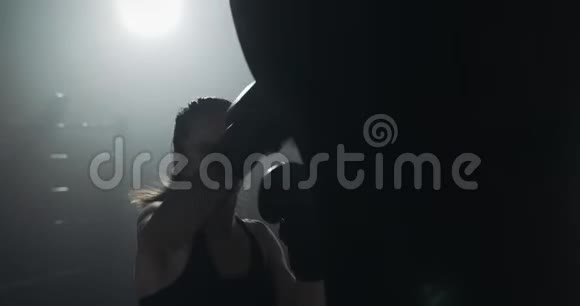 在拳击俱乐部里用拳击袋训练年轻女子的剪影慢动作黑暗的背景视频的预览图