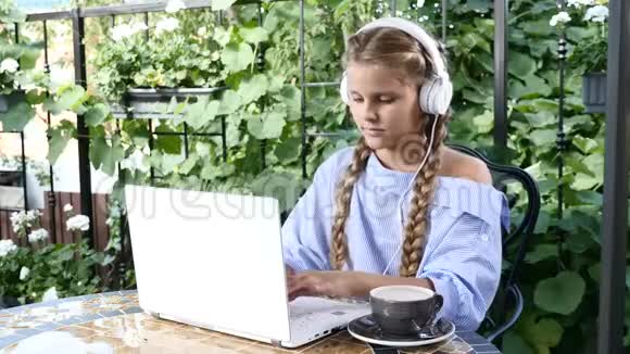 年轻漂亮的女孩坐在一家街头餐馆里桌子上有一台白色笔记本电脑生活方式的概念女生在听视频的预览图