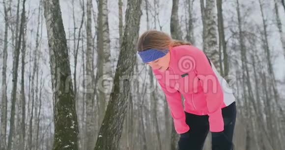 一个年轻女子在冬林里晨跑时累了停下来喘口气他恢复了体力视频的预览图