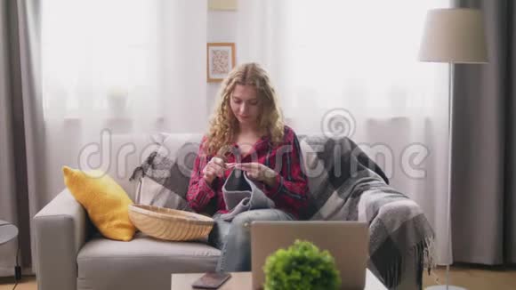 坐在沙发上在舒适的家编织衣服的女人视频的预览图