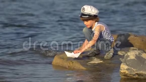 在海滩上用纸船下水的孩子小男孩把纸船放在海面上航行的船梦想未来视频的预览图