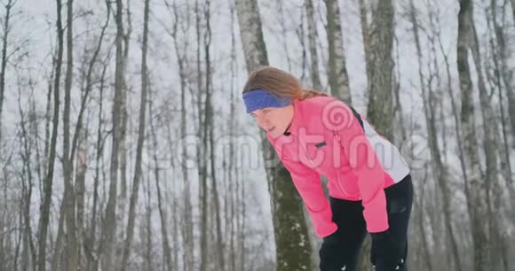 一个年轻女子在冬林里晨跑时累了停下来喘口气他恢复了体力视频的预览图