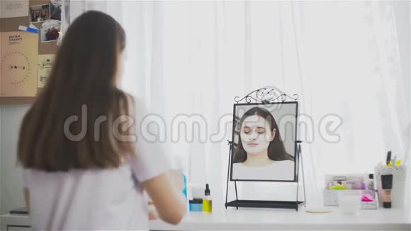 年轻女孩在镜子前的房间里戴着化妆面具视频的预览图