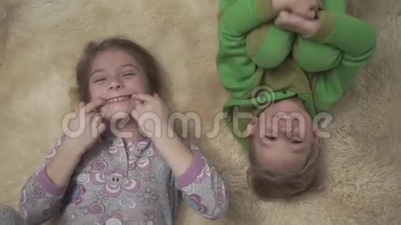 穿着睡衣的快乐小孩子躺在地板上铺着蓬松的地毯兄妹俩在一起玩得很开心快乐视频的预览图