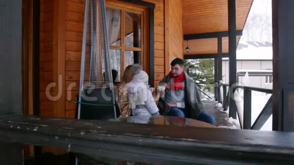一个年轻的家庭带着一个小婴儿在一所漂亮的房子的阳台上喝着热饮视频的预览图