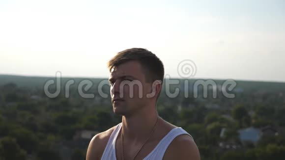 在城市景观背景下坐在屋顶上的年轻快乐男人的肖像英俊的微笑男人看着镜头视频的预览图